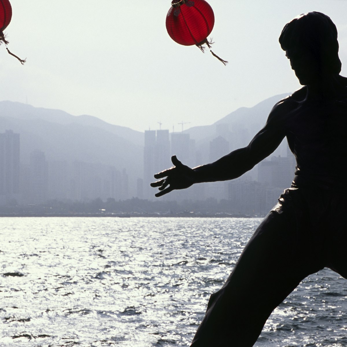 China, Hong Kong, Kowloon. A statue of Cult figure Bruce Lee is silhouetted on the Hong Kong waterfront. The Avenue of the Stars on the Tsim Sha Tsui East Promenade pays homage to the stars of the Hong Kong film industry.