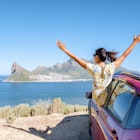 woman outside car window road trip with hands up, car at Chapmans Peak Drive in Cape Town South Africa looking out over the ocean.
1371109801