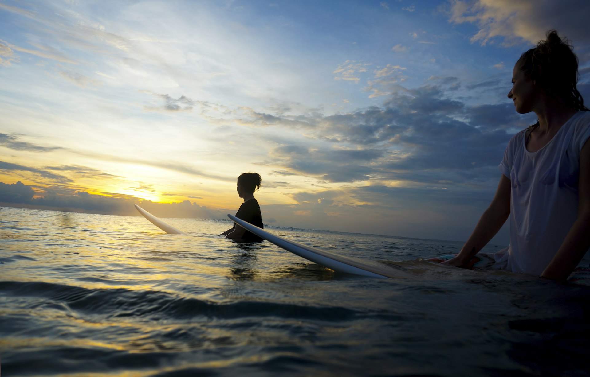 Indonesia, Bali, Canggu, two female surfers in the water watching the sun