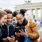 A group of friends travelling together are exploring the local tourist attractions and architecture, they stop for a moment to look over recent photos on their phones.