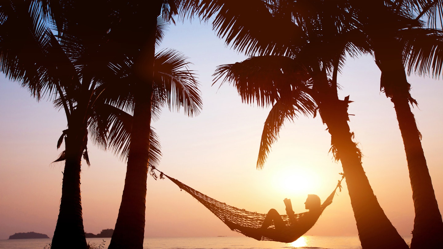 Silhouette of a woman relaxing in a hammock on a beach during sunset. 