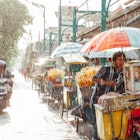 Ubud, Indonesia - March 08, 2016: Indonesian food vendor hides from the rain under the ​umbrella of his stall on the street of Kuta, Bali, Indonesia on March 08, 2016