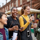 A group of friends walk  through a city street holding coffee cups. 