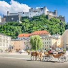 Beautiful panoramic view of the historic city of Salzburg with traditonal horse-drawn Fiaker carriage and famous Hohensalzburg Fortress on a hill on a sunny day with blue sky and clouds in summer; Shutterstock ID 1038459445; your: Claire Naylor; gl: 65050; netsuite: Online Editorial; full: Best places to visit Austria
